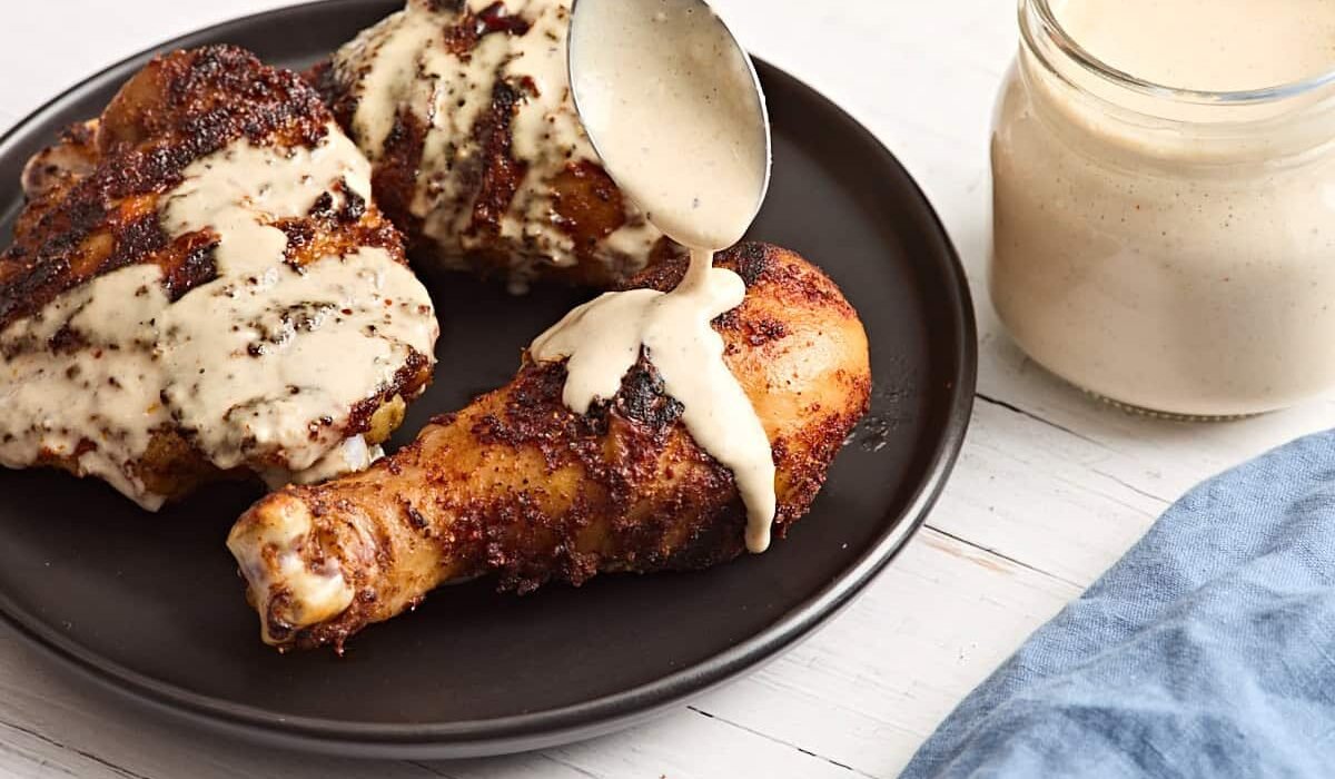 Alabama white sauce being spooned over a grilled chicken drumsticks.