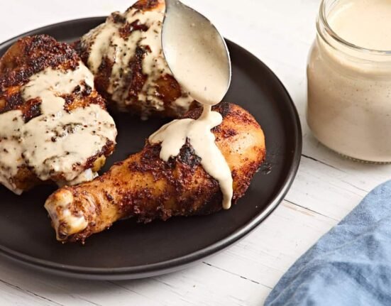 Alabama white sauce being spooned over a grilled chicken drumsticks.